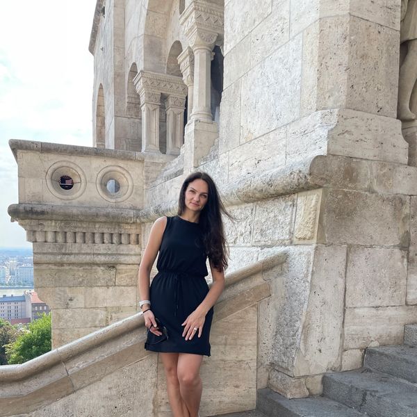 Woman in a black dress posing by historic stone architecture outdoors.