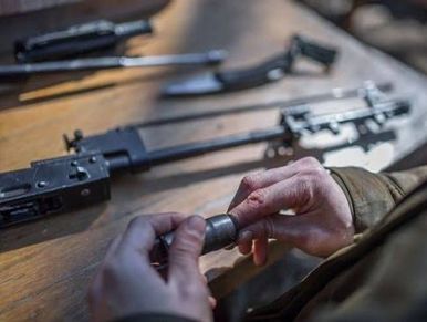 Hands assembling a firearm on a wooden table.