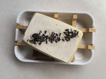 Handmade bar soap with dried lavender buds on a wooden rack in a white dish.