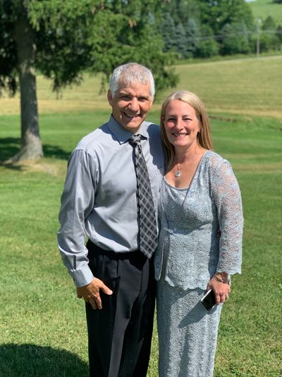 Smiling couple dressed formally outdoors on a sunny day.
