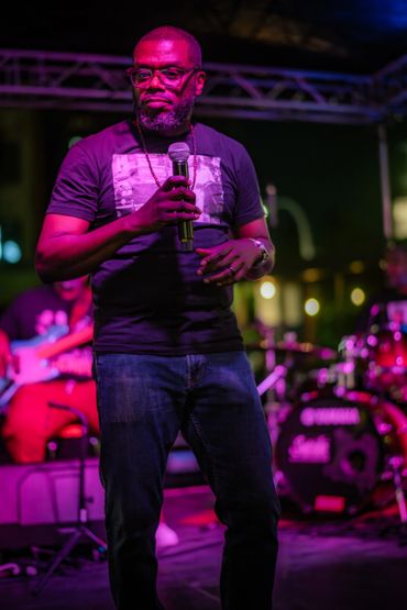 Man holding microphone on stage during a nighttime performance.