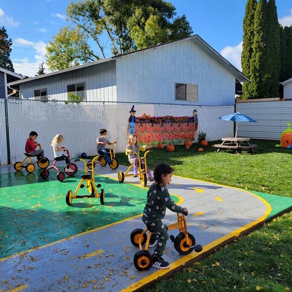 Children riding tricycles in a sunny playground with fall decorations.