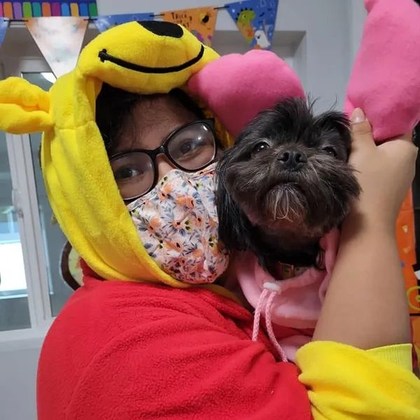 Person in a Winnie the Pooh costume holding a small dog in pink clothes.