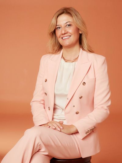 Confident woman in a stylish pink suit smiling against a peach background.