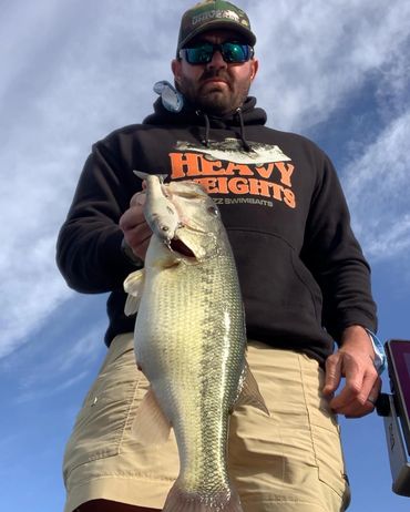 Man holding a large fish outdoors under a blue sky.
