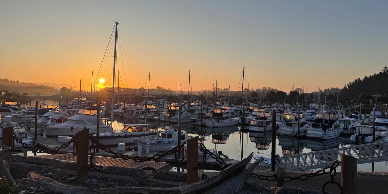 Sunset over a marina filled with docked boats and calm water reflections.