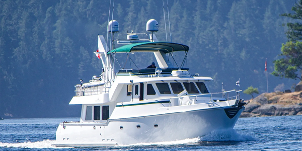 A white motor yacht cruising in blue waters near a forested shore.