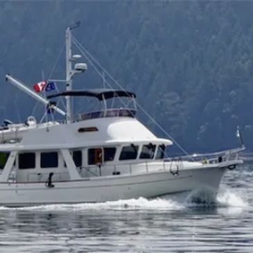 A white motor yacht cruising on calm water with forested hills in the background.