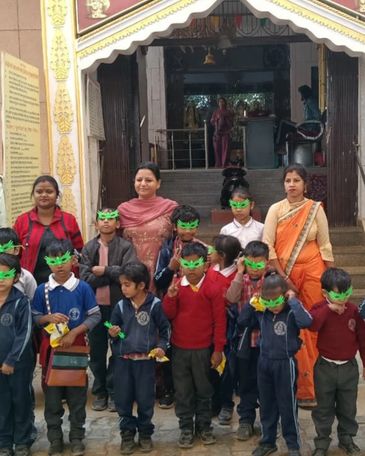 Group of children and teachers outside a temple, children wearing green eye masks.