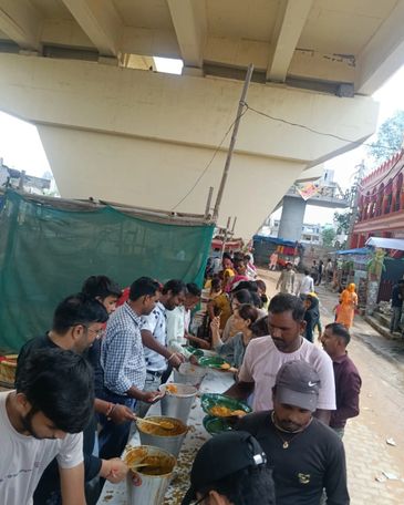 People serving and receiving food in a street under a bridge.