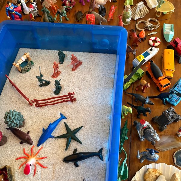 A sand-filled blue tub with toy sea animals and plastic figures on a table.