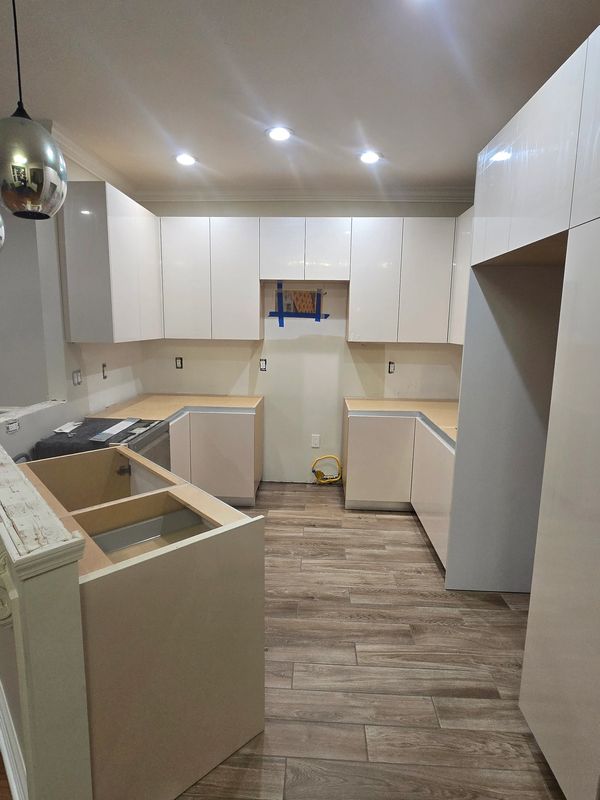 Modern kitchen under construction with white cabinets and wood-look tile flooring.