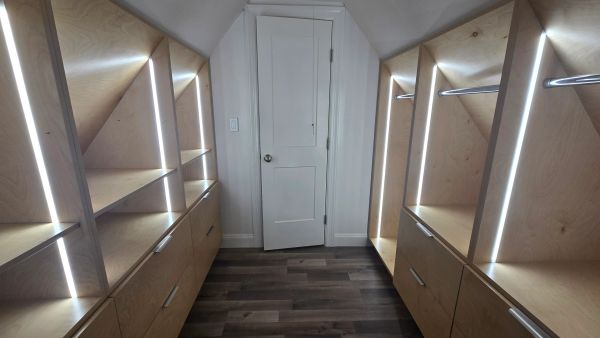 Modern walk-in closet with wooden shelves and LED lighting.