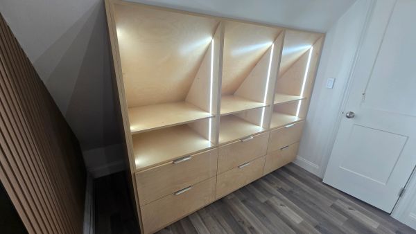 Modern lighted wooden shelving unit with drawers.