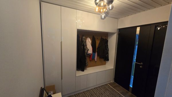 Modern hallway with white cabinets, coat hooks, and a black door.