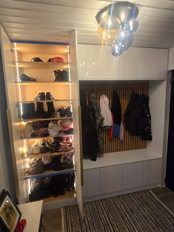 A neatly organized modern closet with shoes, coats, and a stylish light fixture.