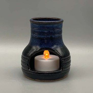 A dark blue ceramic candle holder with a lit tealight candle.