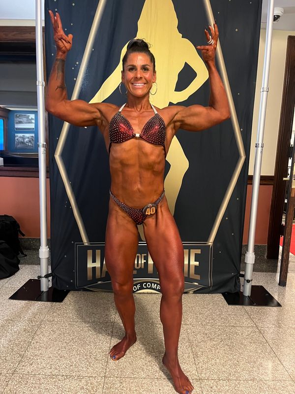 Female bodybuilder posing with arms raised and smiling.