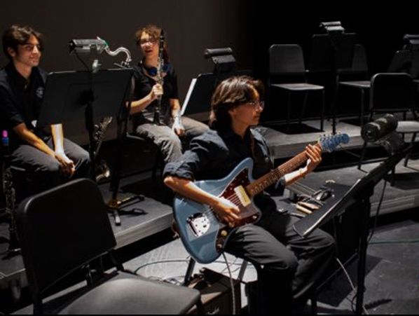 Young musicians rehearsing in a dimly lit room with guitars and clarinets.