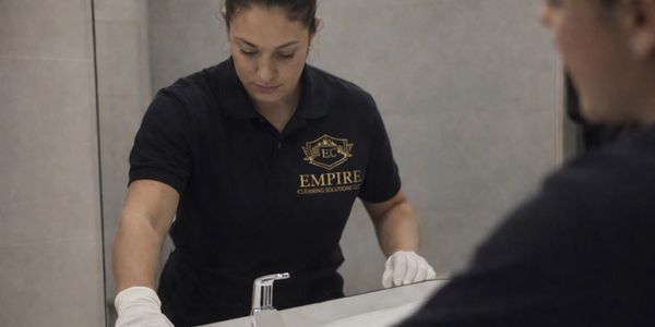 Professional cleaner wiping bathroom sink with gloves on.