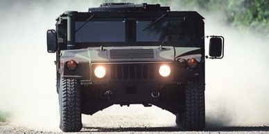 Military Humvee vehicle driving on dusty road with headlights on.