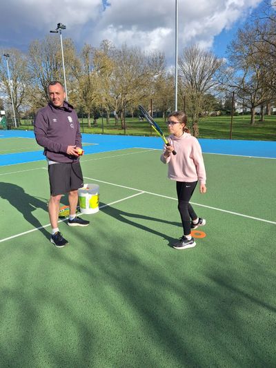 A man coaching a young girl in tennis on an outdoor court.