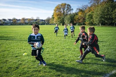 Young boys playing rugby on a sunny day in a green field.