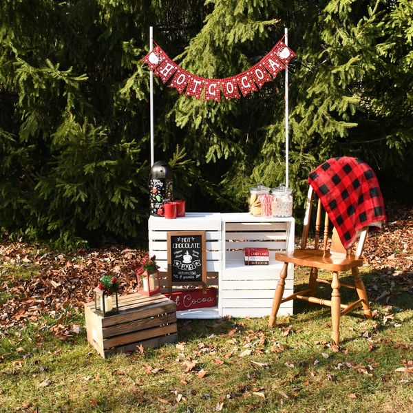 Outdoor hot cocoa stand with festive decorations and a wooden chair.