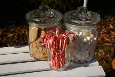 Glass jars filled with cookies, marshmallows, and candy canes on a white table.