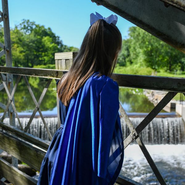 Girl in a blue cape standing on a bridge overlooking a waterfall.