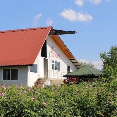 White building with a red roof surrounded by greenery under a blue sky.