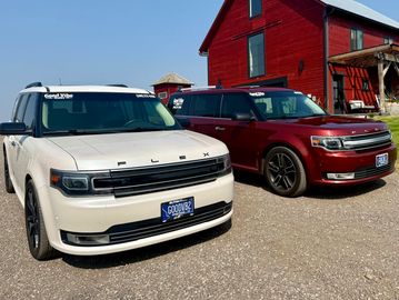 Two Ford Flex SUVs parked outside a red building.