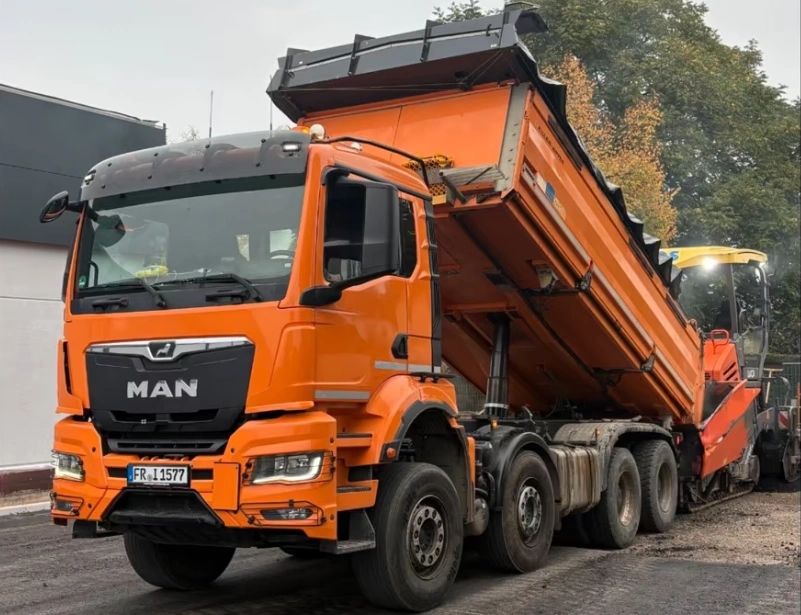 Bright orange MAN dump truck unloading asphalt for road construction.