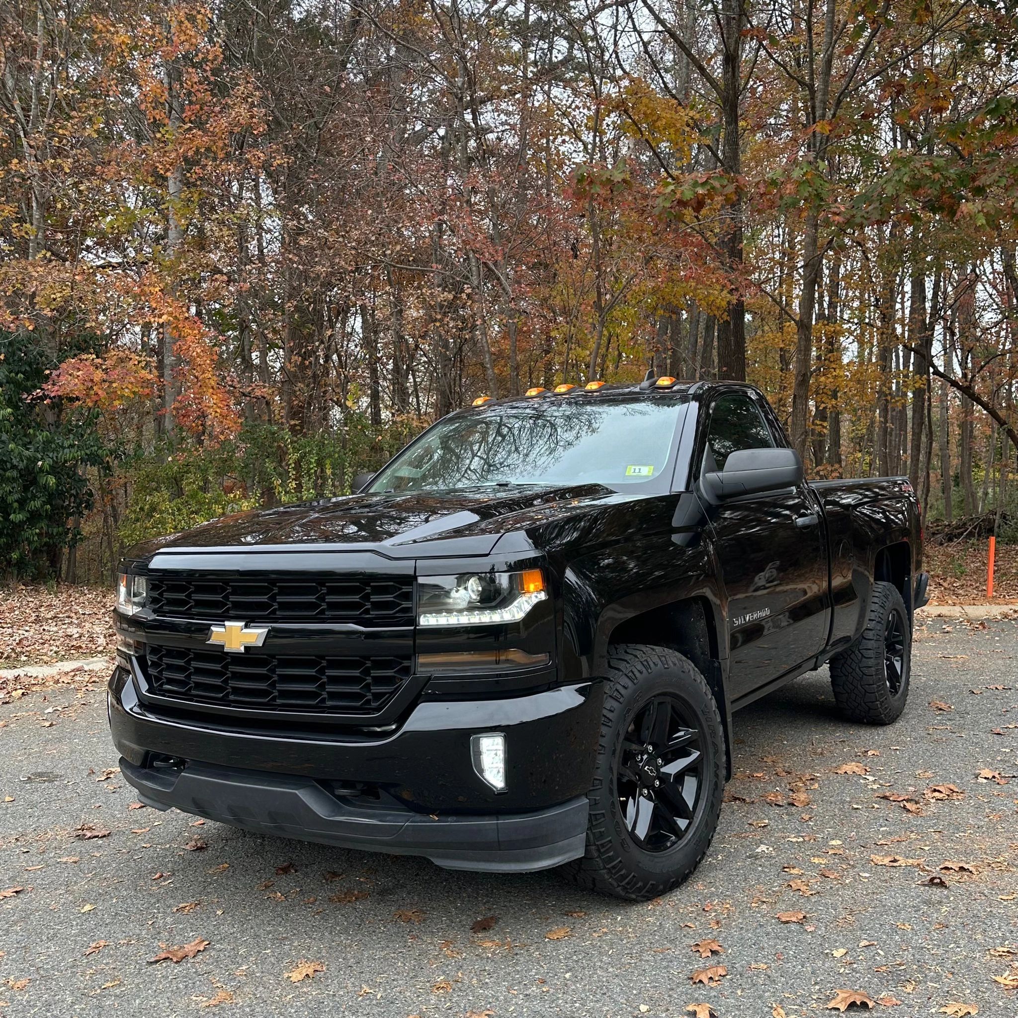 Black Chevrolet Silverado truck in a wooded area.