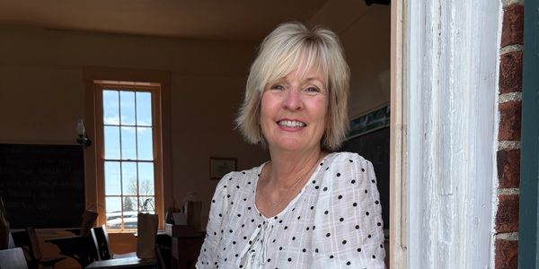Smiling woman in a white polka dot blouse at a doorway.