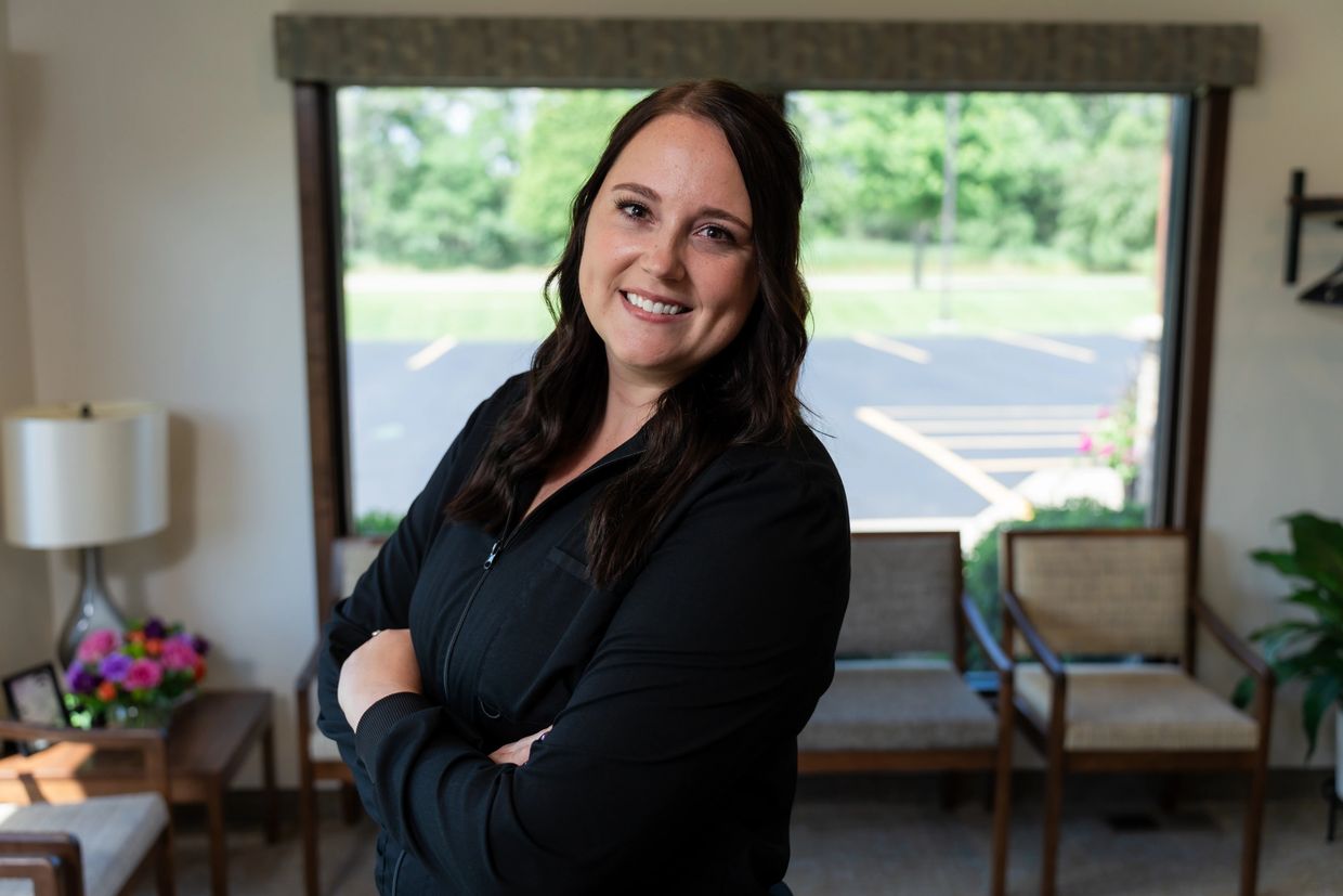Smiling woman with dark hair in a black jacket stands confidently indoors.