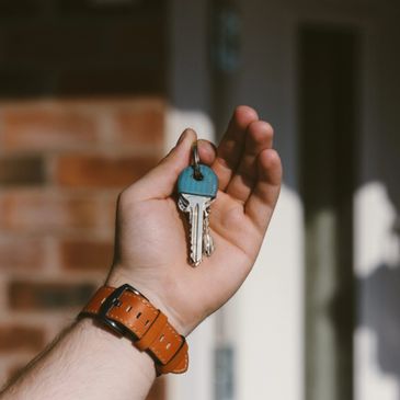 White Hand Holding House Keys In front Of Home