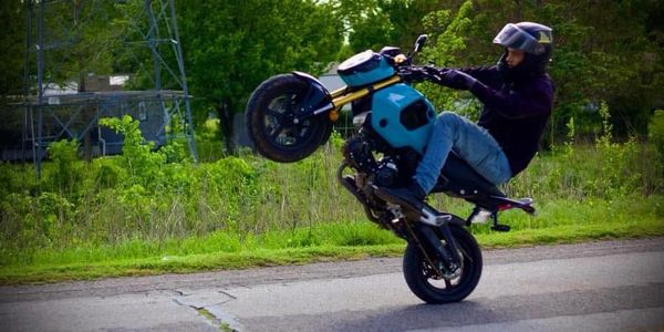 Person performing a wheelie on a blue motorcycle on a road.
