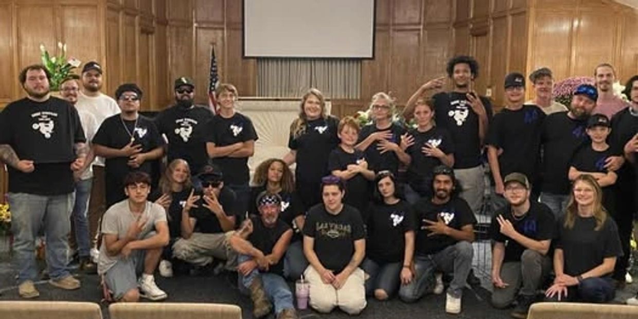 A large group posing in a wood-paneled room, many wearing matching black shirts.