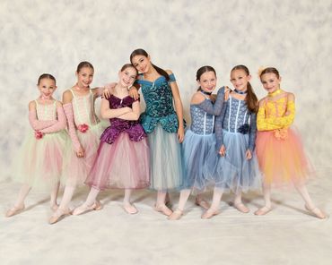 Seven young ballerinas in colorful tutus posing together.