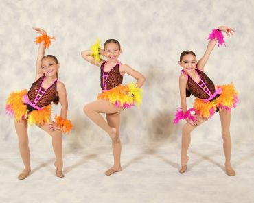 Three young dancers in colorful costumes striking poses.