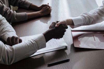 Two people shaking hands over a wooden table with documents.