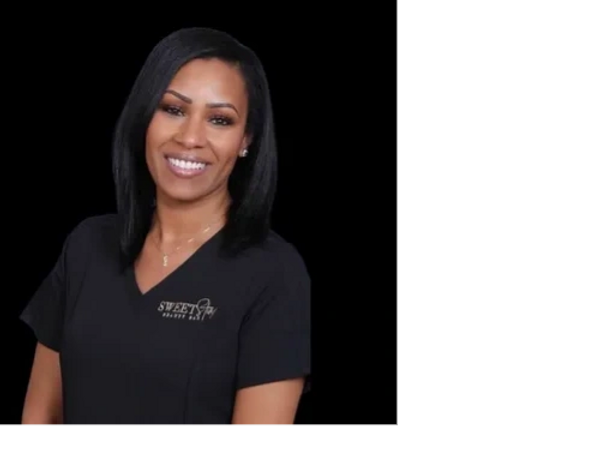 Smiling woman in black medical scrubs against a black background.