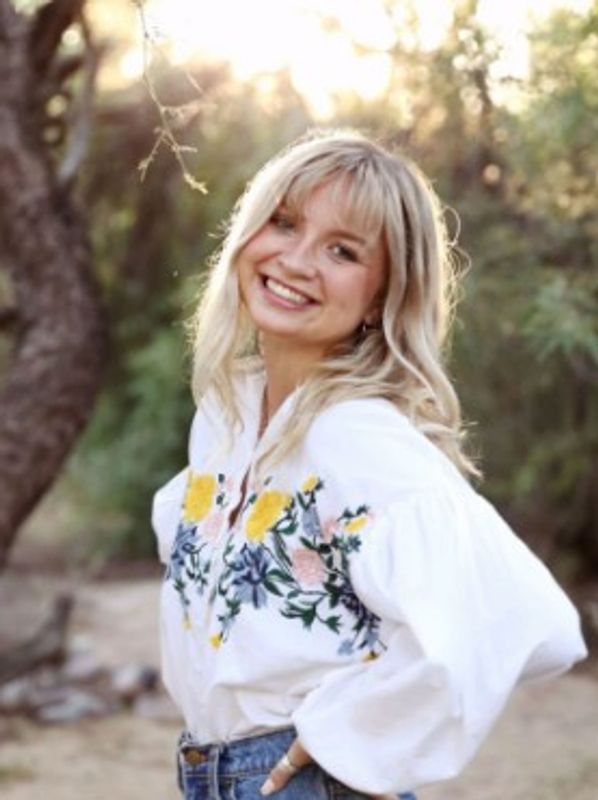 Smiling woman outdoors in a floral embroidered blouse.