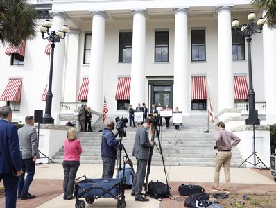 Group of people gathered outside a building with cameras and speakers.
