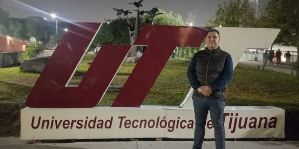 Hombre de pie frente al letrero de la Universidad Tecnológica de Tijuana por la noche.