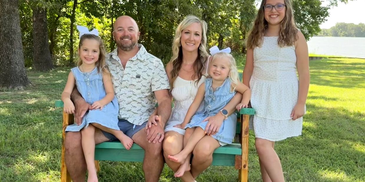 Happy family sitting on bench outdoors with greenery and lake.