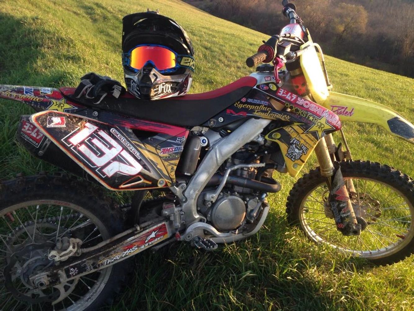 A dirt bike with a helmet resting on the seat in a grassy field.