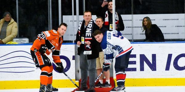 Two ice hockey players face off as officials prepare for the puck drop.