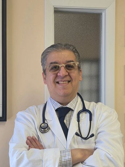 Smiling male doctor with glasses and stethoscope, arms crossed.